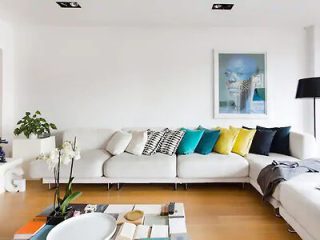Spacious modern living room with white sofa, colorful cushions, and large windows allowing natural light